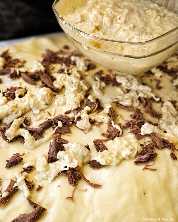 Unbaked cookie dough spread with white chocolate drizzle and dark chocolate shavings ready to bake